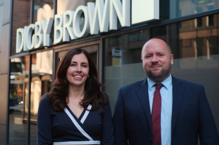Hannah Bennett and Craig Smillie standing in front of the Digby Brown Glasgow office smiling