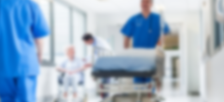 A hospital corridor with staff walking, one is pushing a hospital bed - the image is blurred.